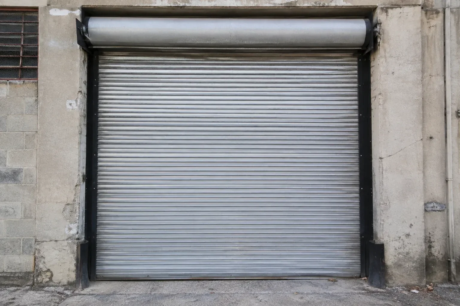 Closed metal rolling shutter in a weathered warehouse opening. — Commercial Rolling Door Repair, Innisfil