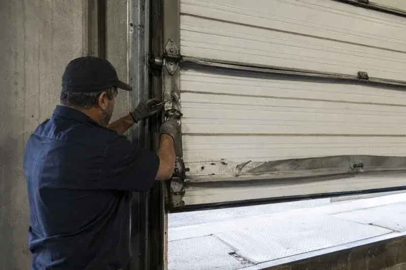 Person holding tools at the side hinge of a partly raised industrial sectional door — Commercial Sectional Door Repair, Innisfil