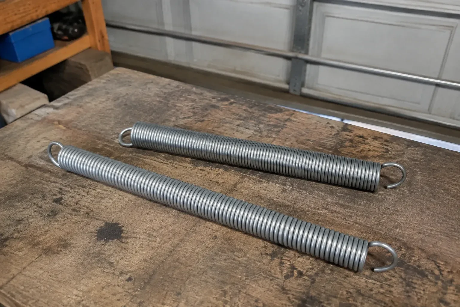 Two detached extension springs with hooked ends on a garage bench. — Extension Spring Replacement, Innisfil Park