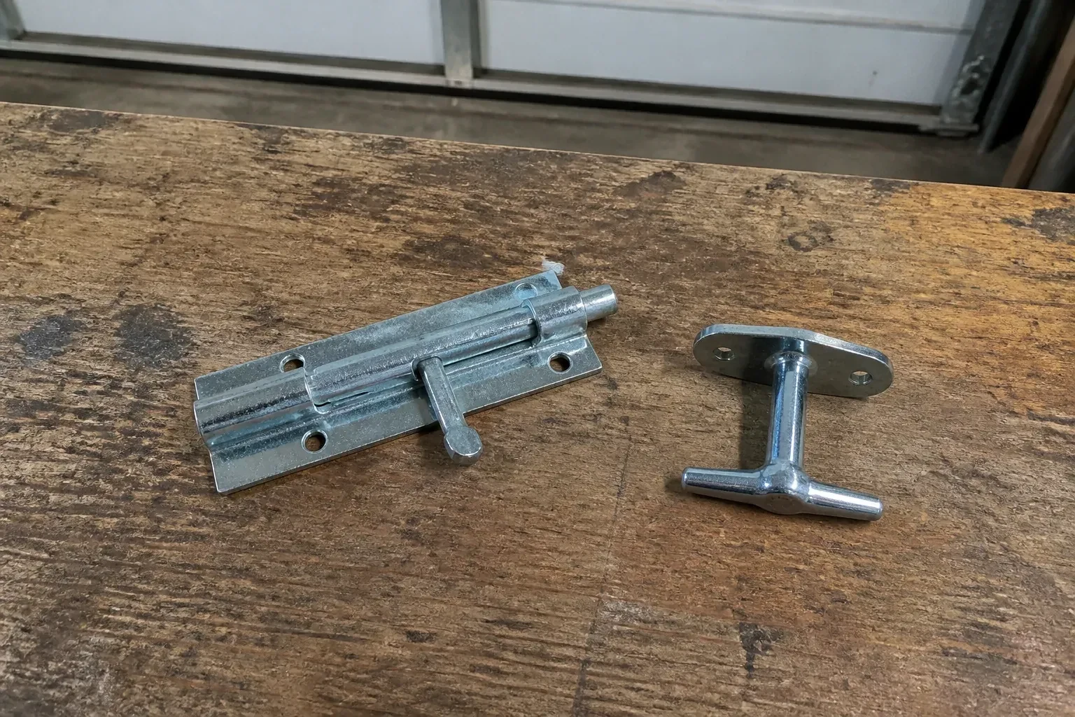 Detached slide bolt and T-handle on a wooden garage workbench. — Garage Door Manual Lock Repair, Innisfil